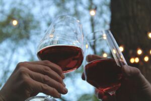 Mains de deux personnes qui trinquent avec un verre de vin rouge - Photo de rikkia hughessur https://unsplash.com/fr/photos/personne-tenant-un-verre-de-vin-transparent-avec-du-vin-rouge-aYKPc05ozp4