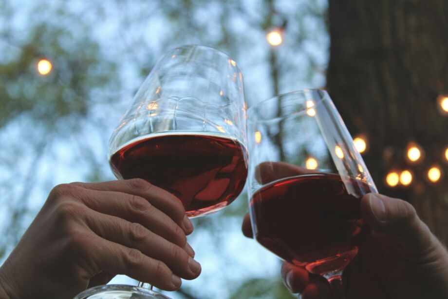 Mains de deux personnes qui trinquent avec un verre de vin rouge - Photo de rikkia hughessur https://unsplash.com/fr/photos/personne-tenant-un-verre-de-vin-transparent-avec-du-vin-rouge-aYKPc05ozp4