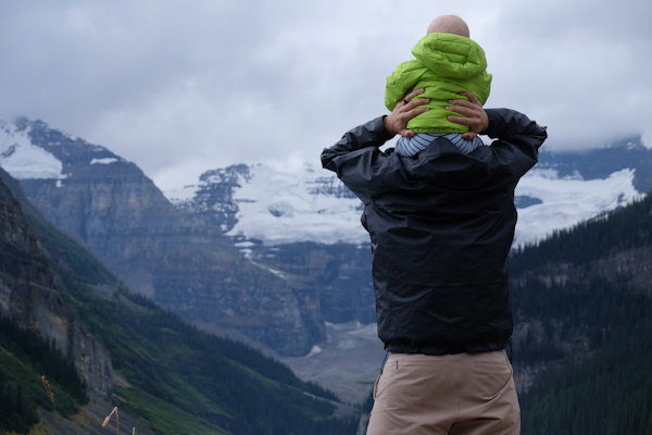 Un père porte son fils sur les épaules devant un paysage de montagnes - Photo by Austin Walker on Unsplash