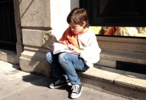 Un enfant, lisant la Bible, assis sur des marches dans la rue - photo par Marc Pernot