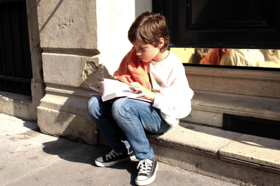 Un enfant, lisant la Bible, assis sur des marches dans la rue - photo par Marc Pernot