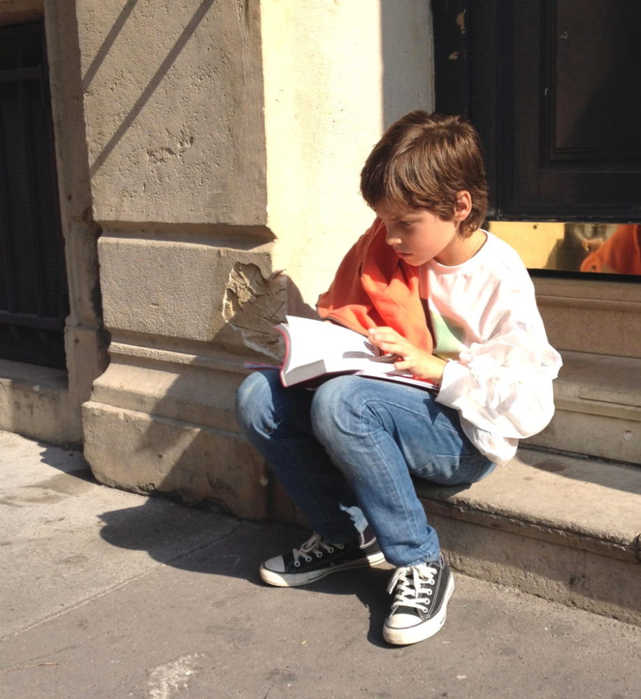 Un enfant, lisant la Bible, assis sur des marches dans la rue - photo par Marc Pernot
