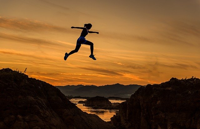 une jeune femme saute par dessus une vallée, sur un fond de coucher de soleil - Image par Sasin Tipchai de Pixabay
