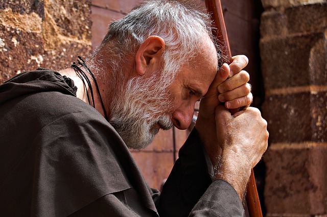 un moine âgé, debout, en prière ou en pensée, appuyé sur un bâton - Image par Qrry de Pixabay