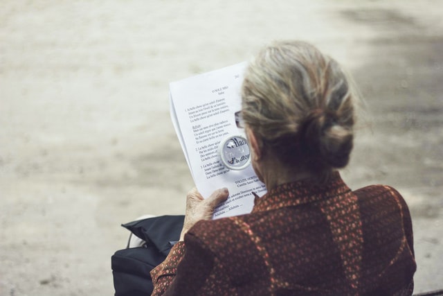 une dame âgée lit un poème de Saint Saens avec une loupe - Photo by Clément Falize on Unsplash