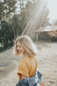 jeune femme souriante, se retourne, éclairée par un rayon de soleil - Photo by Gian Cescon on Unsplash