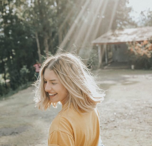 jeune femme souriante, se retourne, éclairée par un rayon de soleil - Photo by Gian Cescon on Unsplash