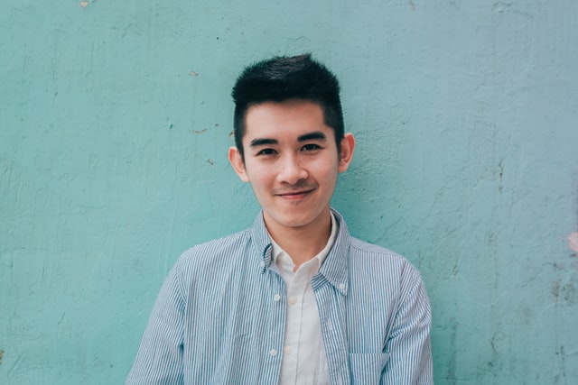 Un jeune souriant devant un mur peint en vert - Photo by JD Chow on Unsplash
