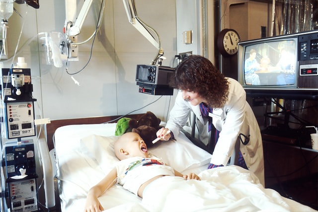 Une médecin se penche vers un enfant qui montre sa gorge dans un hôpital contre le cancer - Photo by National Cancer Institute on Unsplash