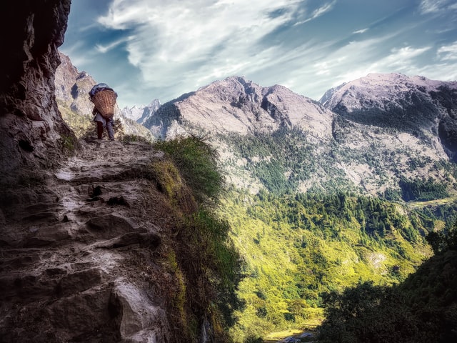 un paysan porte une lourge charge sur un chemin de montagne - Photo by Simon Berger on Unsplash