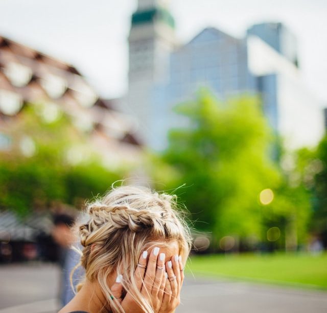femme blonde se cachant le visage avec en arrière fond une église - Photo by Abigail Keenan on Unsplash