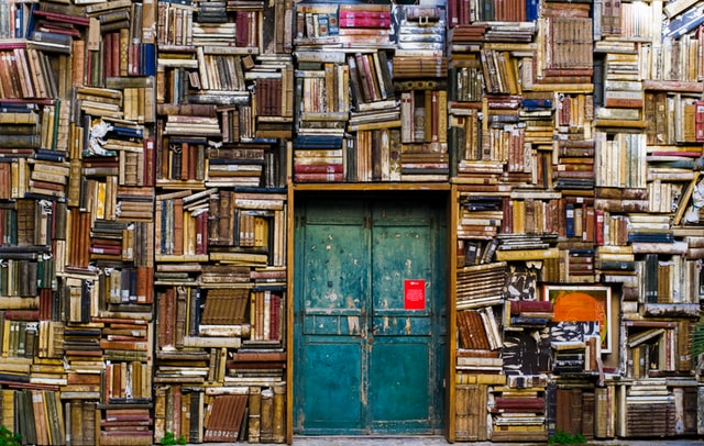 un mur couvert de livres entourant une porte fermée - Photo by Eugenio Mazzone on Unsplash