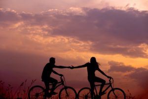une femme devance un homme en vélo et tente de le ratrapper, sur fond de coucher de soleil - Photo by Everton Vila on Unsplash