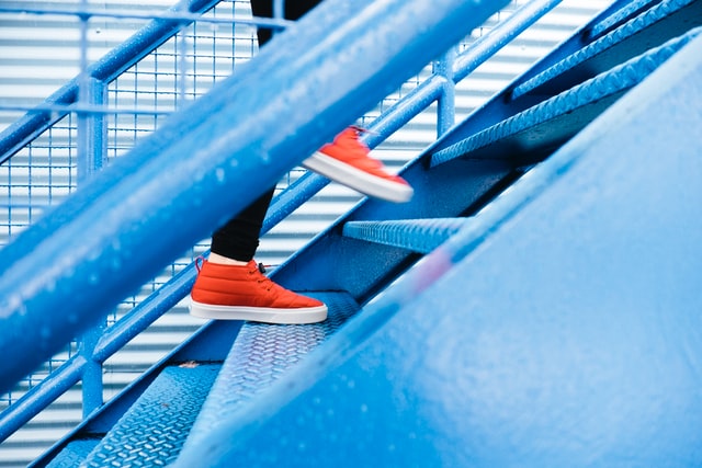 des jambes avec jean et baskets rouges montent un escalier en métal bieu - Photo by Lindsay Henwood on Unsplash