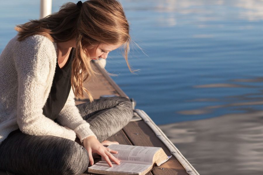 jeune femme lisant la Bible sur un ponton (recadrée) - Bethany Laird sur https://unsplash.com/fr/photos/photo-dune-femme-lisant-un-livre-pres-dun-plan-deau-vGReyBvIX-o