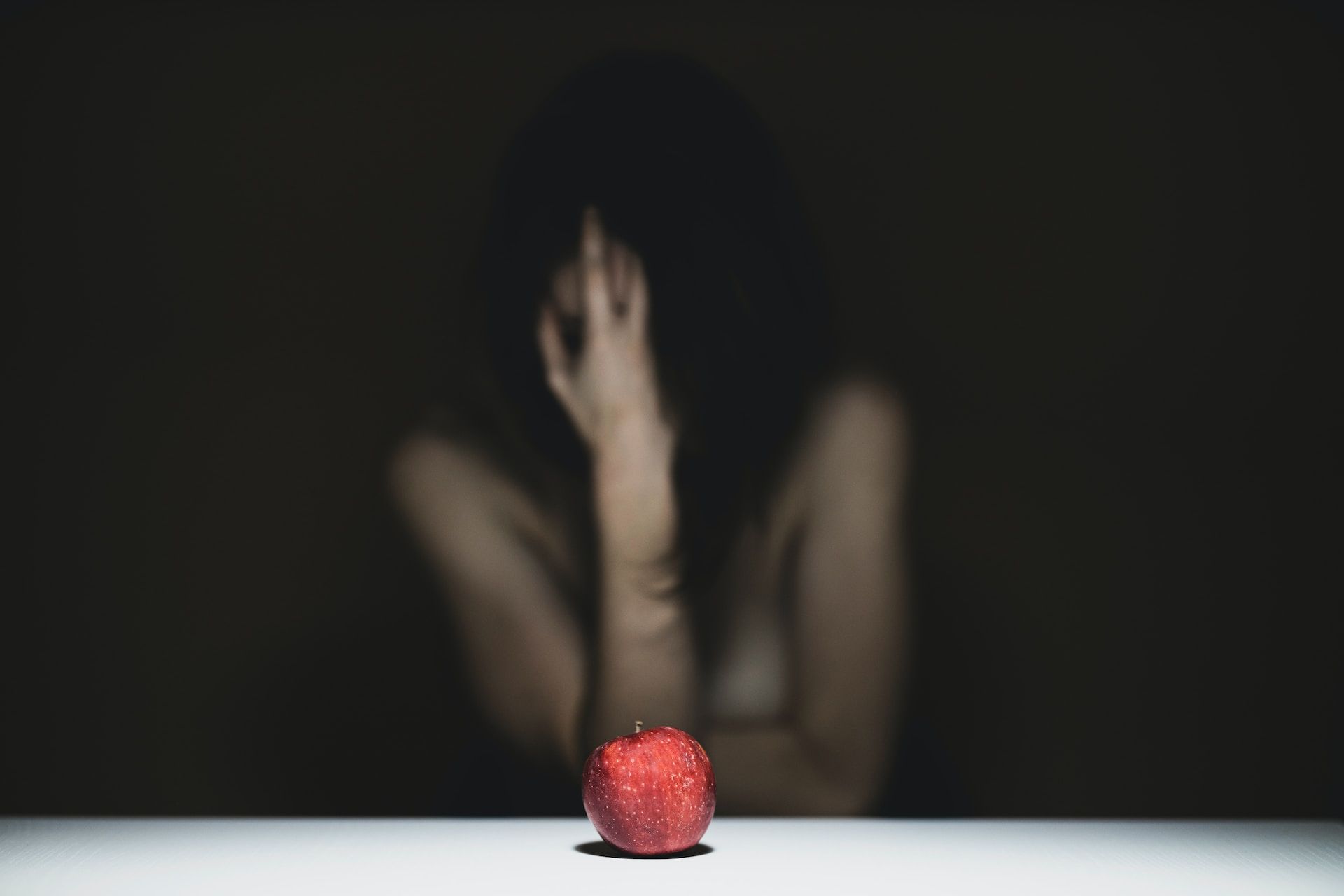 Gros plan sur une pomme avec une femme nue derrière se prenant la tête - Photo by engin akyurt on https://unsplash.com/fr/photos/femme-se-couvrant-le-visage-avec-de-la-pomme-rouge-ZeuDhLpjgsA