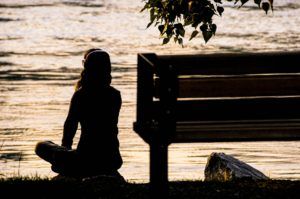 Une femme seule, assise sur le bord d'une rivière au coucher du soleill, un casque sur les aoreilles - Photo by Toni Reed on Unsplash