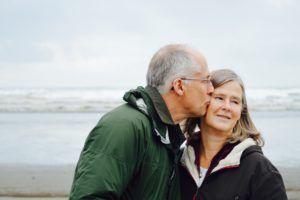 Un couple de personne d'âge moyen en bord de mer, le mari pose un baiser sur la joue de sa femme qui détourne de regard - Photo by Esther Ann on Unsplash