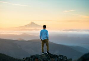 Une personne au sommet d'une montagne regarde l'aube sur une mer de nuages - Photo de Tim Bogdanov sur https://unsplash.com/fr/photos/homme-debout-au-sommet-de-la-montagne-4uojMEdcwI8
