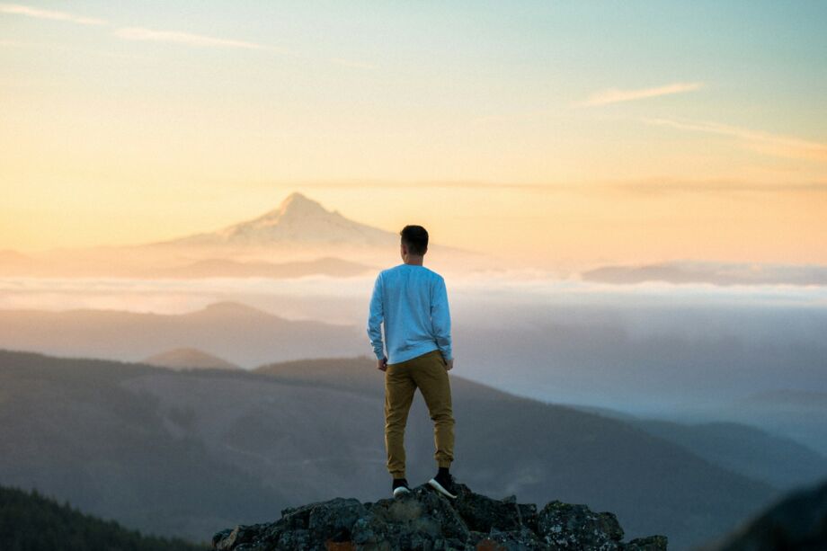 Une personne au sommet d'une montagne regarde l'aube sur une mer de nuages - Photo de Tim Bogdanov sur https://unsplash.com/fr/photos/homme-debout-au-sommet-de-la-montagne-4uojMEdcwI8