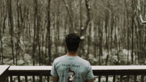 Un homme regarde la neige tomber, avec un tee-shirt évoquant le serpent de la tentation - Photo by Scott Broome on Unsplash
