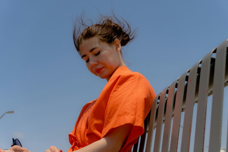 Une jeune femme en orange vif est assise sur un banc, médite en regardant vers le bas - Photo de Zulfugar Karimovsur https://unsplash.com/fr/photos/une-femme-en-chemise-orange-est-assise-sur-un-banc-a-lexterieur-CKhgz4_XBB0