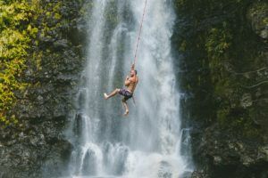 un homme se tenant à une corde à noeuds au dessus d'une chute d'eau - Photo by Derek Owens on Unsplash