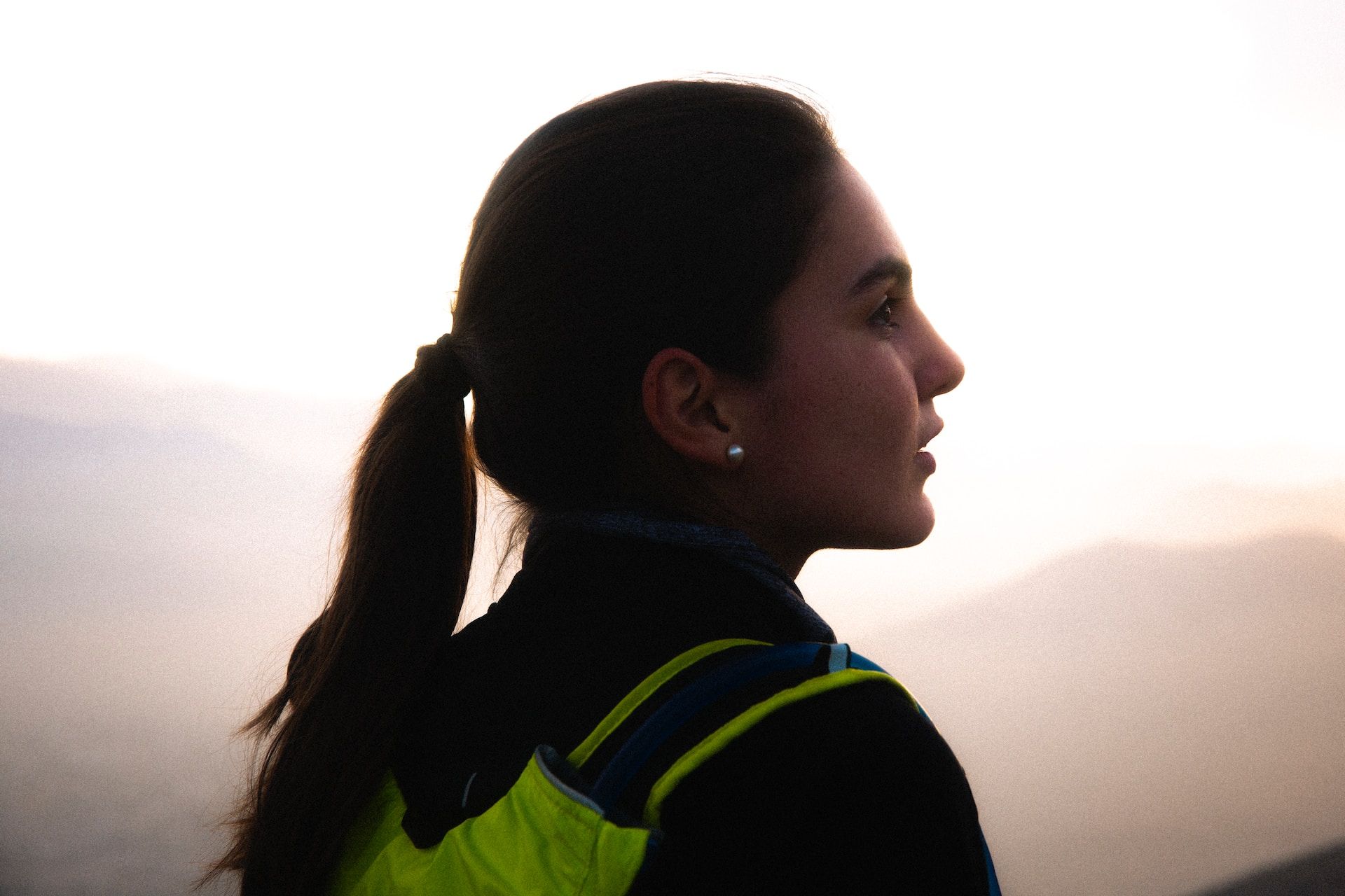 une jeune femme avec un sac à dos, de profil, regarde le lever de soleil en montagne - Photo by Alvaro Palacios on https://unsplash.com/fr/photos/homme-en-sweat-a-capuche-noir-et-vert-embrassant-femme-en-chemise-noire-pxgnpszogp0