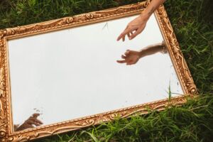 Allusion à la création de l'humain par Michel-Ange : un miroir révèle que nous sommes créés par Dieu et que cette création est en cours - Photo de Chase Kennedy sur https://unsplash.com/fr/photos/une-personne-tendant-la-main-pour-toucher-un-miroir-uvmTg80KJ4o