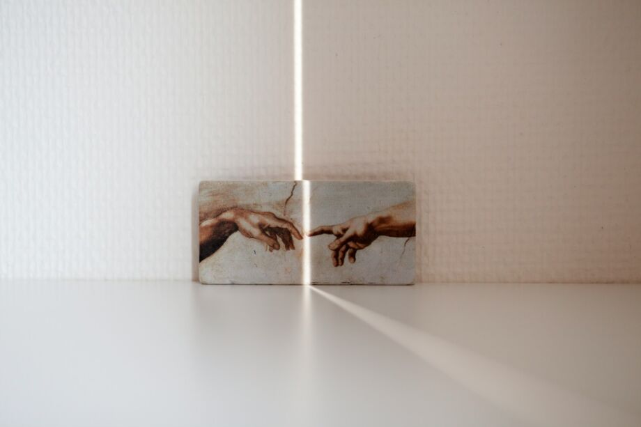 Une reproduction de la fresque de la création de l'humain par Michel-Ange posée sur le sol contre un mur et éclairée d'un rayon de lumière - Photo de Cherry Laithang sur https://unsplash.com/fr/photos/peinture-a-la-main-__pzUnC_OWA