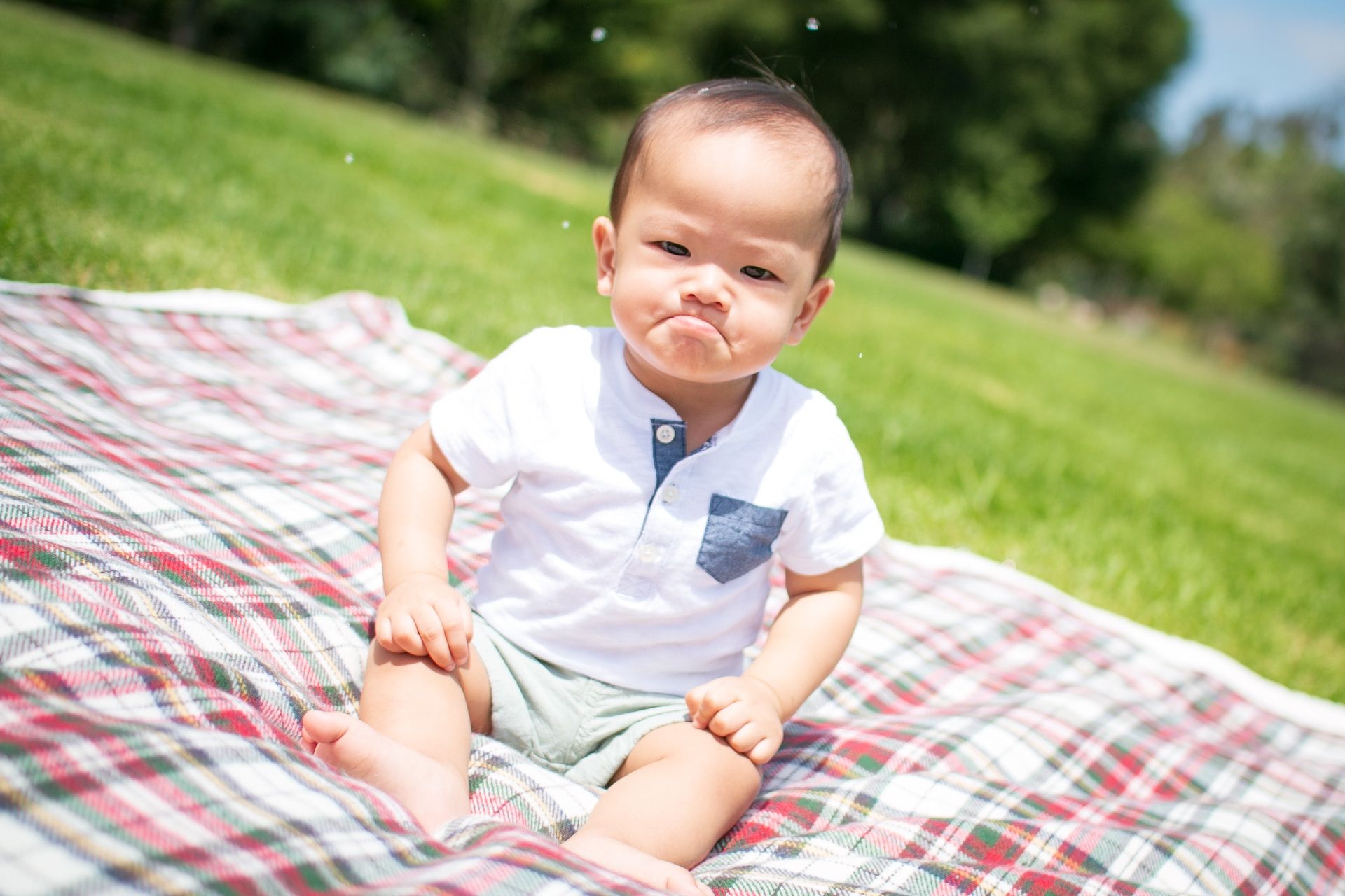 Un bébé qui a l'air en colère, assis sur une nappe de pique-nique dans un parc - Photo by Ryan Franco on https://unsplash.com/fr/photos/photographie-selective-de-mise-au-point-dun-enfant-en-bas-age-au-visage-grincheux-assis-sur-un-coussin-a-carreaux-prise-pendant-la-journee-XECZHb6NoFo