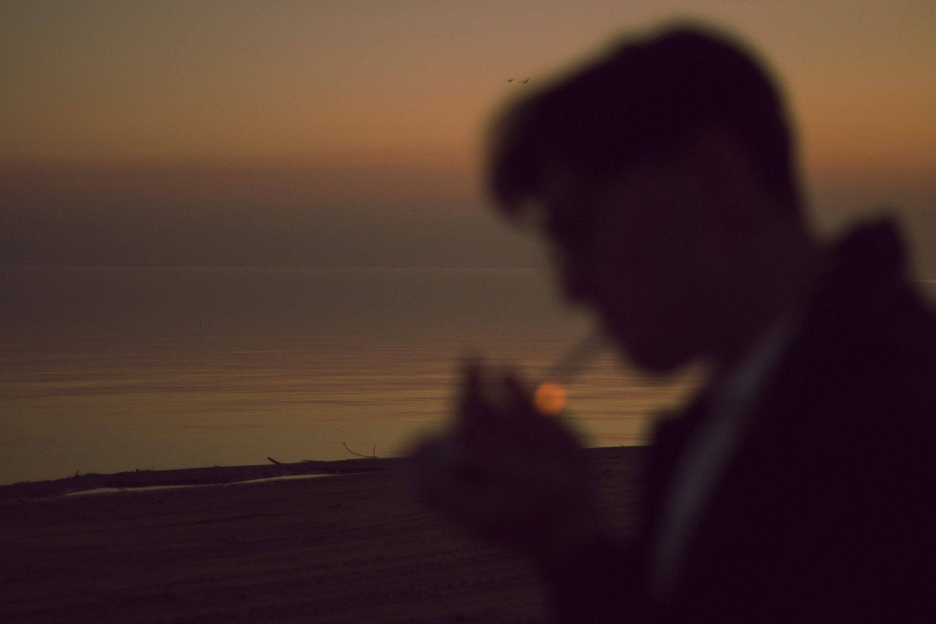 Silhouette d'un homme allumant une cigarette sur fond de coucher de soleil sur la mer - Photo by Zhassulan Zhaynaqov on https://unsplash.com/fr/photos/homme-debout-tout-en-fumant-une-cigarette-pres-dun-plan-deau-InrdPueluSI