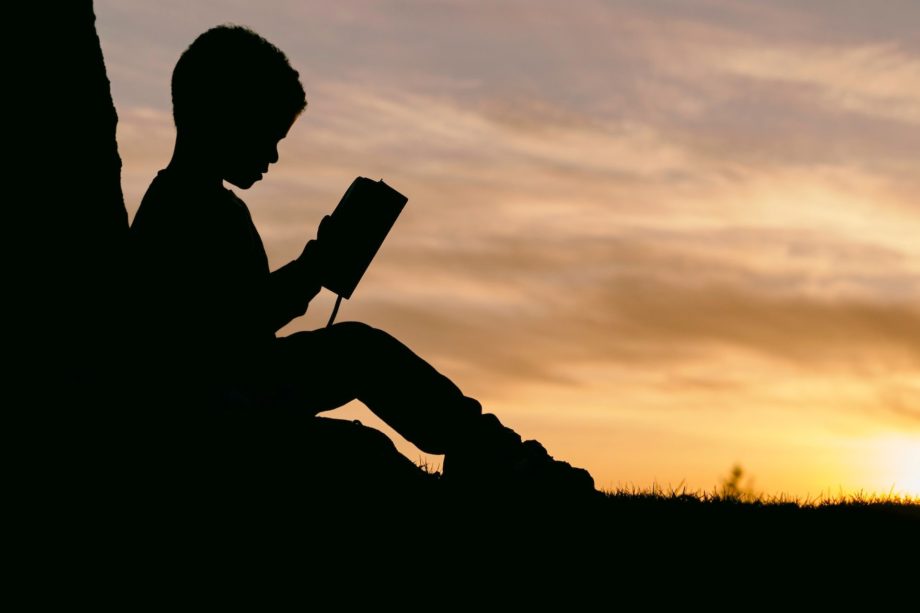 un enfant lisant la Bible contre un arbre - Photo by Aaron Burden on https://unsplash.com/fr/photos/6jYoil2GhVk