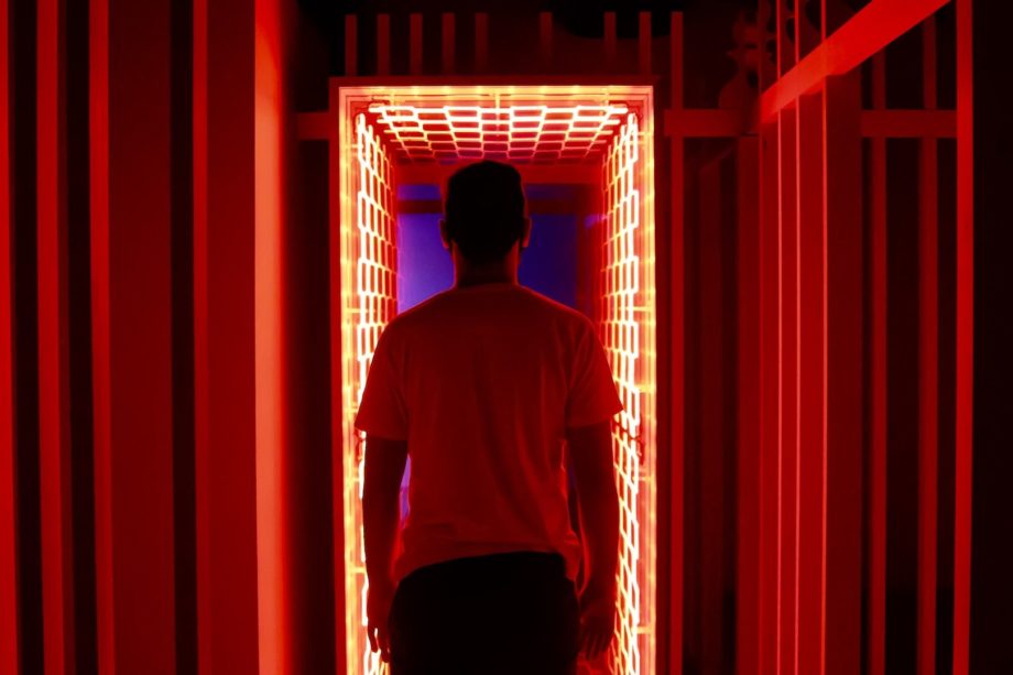 Un homme entre dans un couloir éclairé par des néons rouges - Photo by Nathana Rebouças on https://unsplash.com/fr/photos/homme-en-t-shirt-a-col-rond-blanc-debout-devant-le-rideau-de-fenetre-rouge-TtB2gGKKj2c