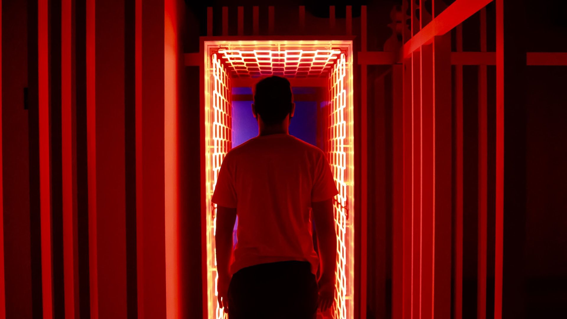 Un homme entre dans un couloir éclairé par des néons rouges - Photo by Nathana Rebouças on https://unsplash.com/fr/photos/homme-en-t-shirt-a-col-rond-blanc-debout-devant-le-rideau-de-fenetre-rouge-TtB2gGKKj2c