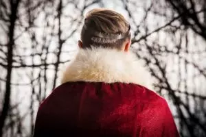 un jeune homme vu de dos en manteau pourpre à col de fourure avec uen couronne en acier - Photo by Paweł Furman on Unsplash