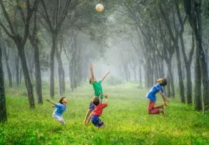 enfants jouant au ballon dans une prairie bordée d'arbres - Photo by Robert Collins on Unsplash 