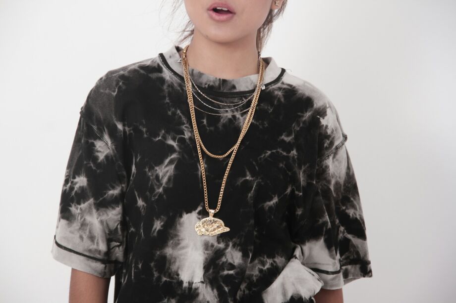 Jeune femme avec un tee-shirt représentant des plumes ou des nuages - Photo de Anton K Wibowo sur https://unsplash.com/fr/photos/une-personne-portant-une-chemise-tie-dye-et-des-chaines-en-or-superposees-DPPGvktbdCQ