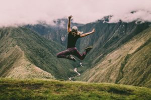 jeune femme sautant d'enthousiasme devant une montagne verte - Photo by Peter Conlan on Unsplash