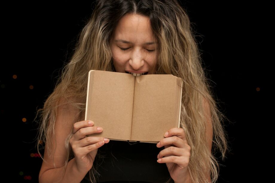 Jeune femme mordant dans un livre - Photo de engin akyurt sur https://unsplash.com/fr/photos/femme-couvrant-son-visage-avec-un-livre-brun-lRcMK6ooaQg