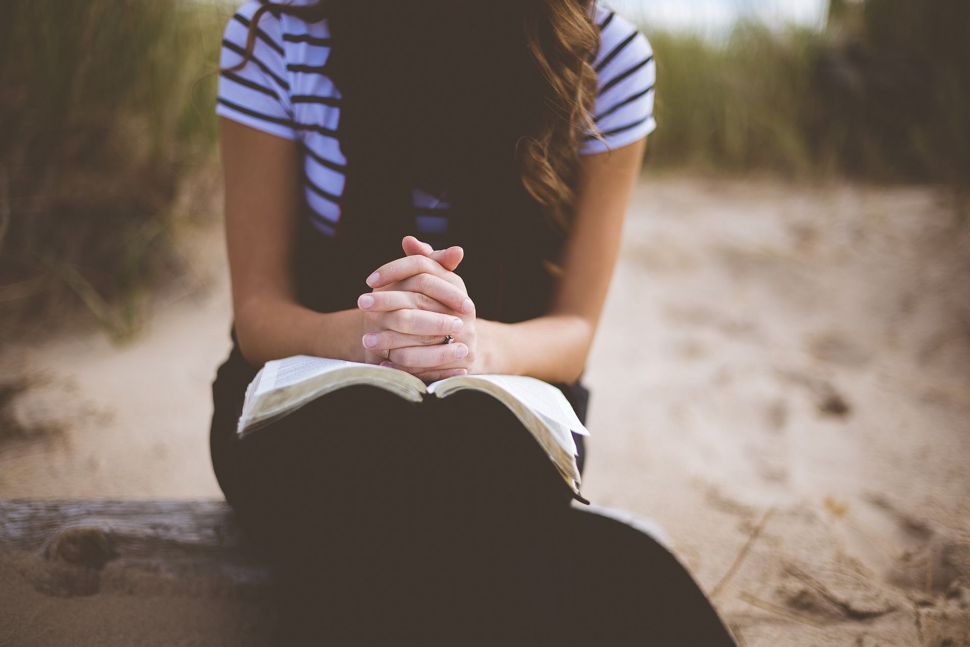 jeune fille priant sur sa Bible. Image par StockSnap de https://pixabay.com/fr/photos/plage-fille-loisirs-en-plein-air-1868772/