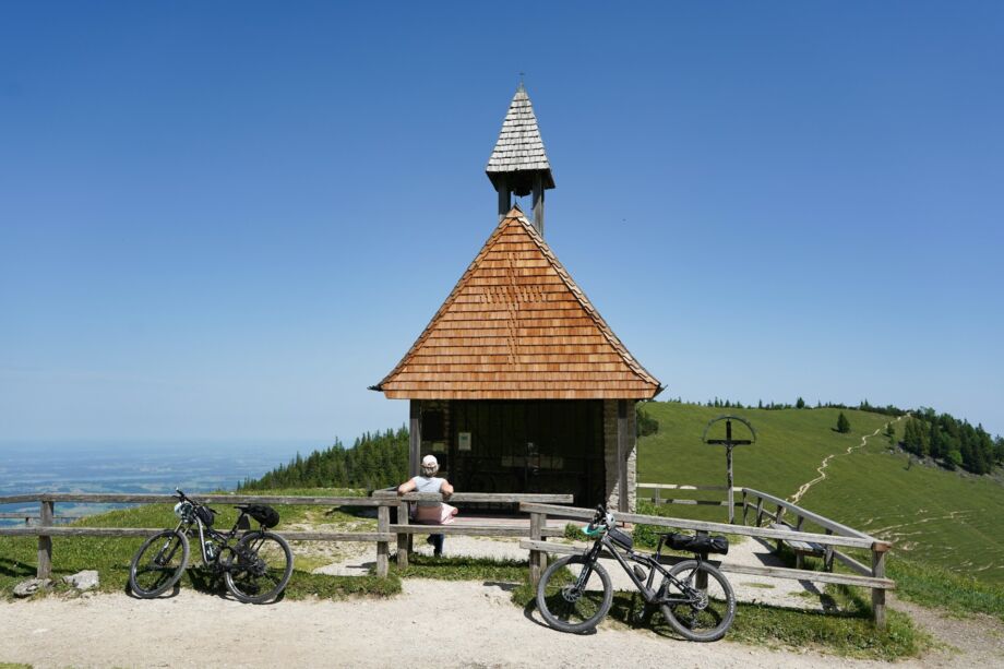 Une personne en vélo s'est assise devant une chapelle de montagne - Photo de Wolfgang Weiser sur https://unsplash.com/fr/photos/petite-chapelle-en-bois-sur-une-montagne-avec-des-velos-xwERkE0uBp8
