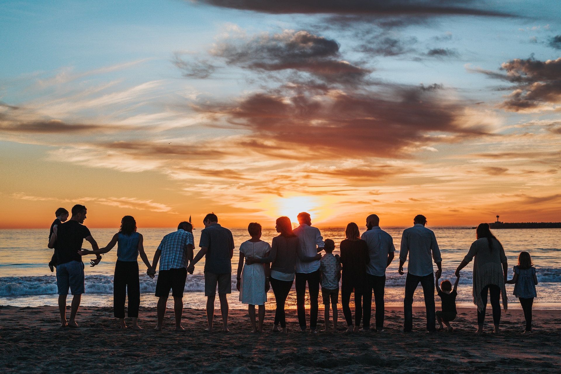 un groupe de personnes d'âges divers se tenant par la main face au soleil couchant sur la mer - Photo by Tyler Nix on https://unsplash.com/photos/V3dHmb1MOXM