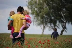 Un père avec deux enfants dan sles bras suivant un troième enfant, dans un champ - Photo by Juliane Liebermann on https://unsplash.com/photos/O-RKu3Aqnsw 