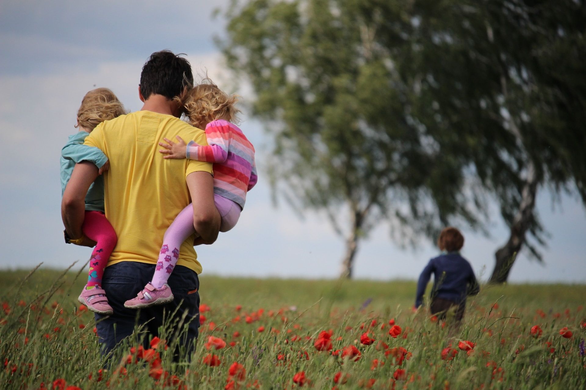 Un père avec deux enfants dan sles bras suivant un troième enfant, dans un champ - Photo by Juliane Liebermann on https://unsplash.com/photos/O-RKu3Aqnsw
