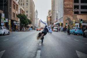 Une jeune femme danse sur une main au centre d'une avenue - Photo de Keenan Constance sur https://unsplash.com/fr/photos/zIwMVgCY8EA 