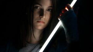 jeune femme tenant une sorte d'épée lumineuse sur un fond d'obscurité - Photo de Some Tale sur https://unsplash.com/fr/photos/femme-en-chemise-grise-a-manches-longues-tenant-une-bouteille-noire-0kAvE08lKK4