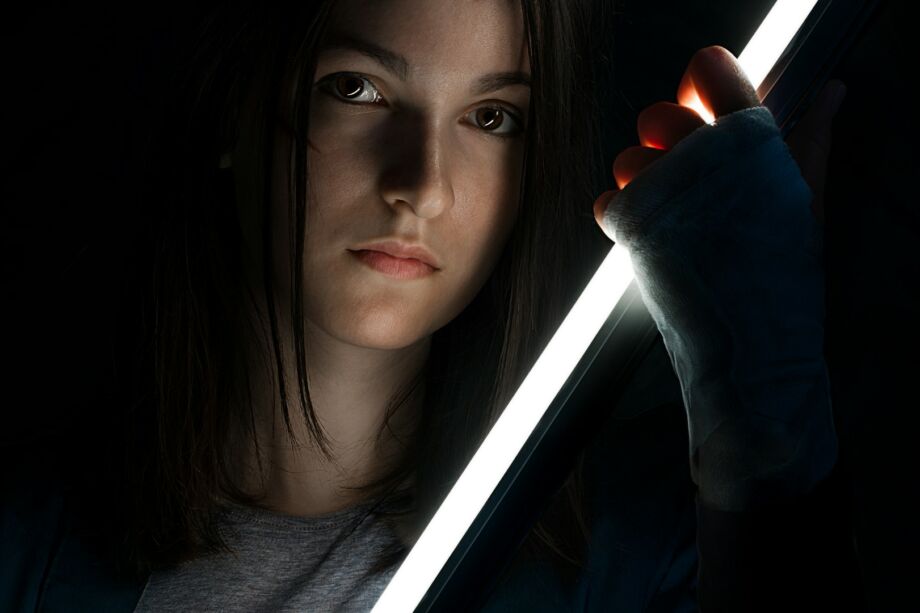 jeune femme tenant une sorte d'épée lumineuse sur un fond d'obscurité - Photo de Some Tale sur https://unsplash.com/fr/photos/femme-en-chemise-grise-a-manches-longues-tenant-une-bouteille-noire-0kAvE08lKK4