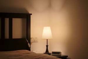 Une lampe allumée au chevet d'un lit vide - Photo de 戸山 神奈 sur https://unsplash.com/fr/photos/hp1kWCABonI 