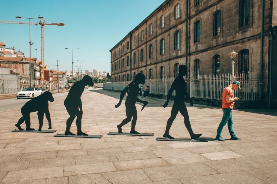des statues en ville représente l'évolution de l'humain, suivi d'un homme penché sur son portable - Photo de Eugene Zhyvchik sur https://unsplash.com/fr/photos/les-personnes-qui-marchent-sur-le-trottoir-pendant-la-journee-xJY-7gtC38o
